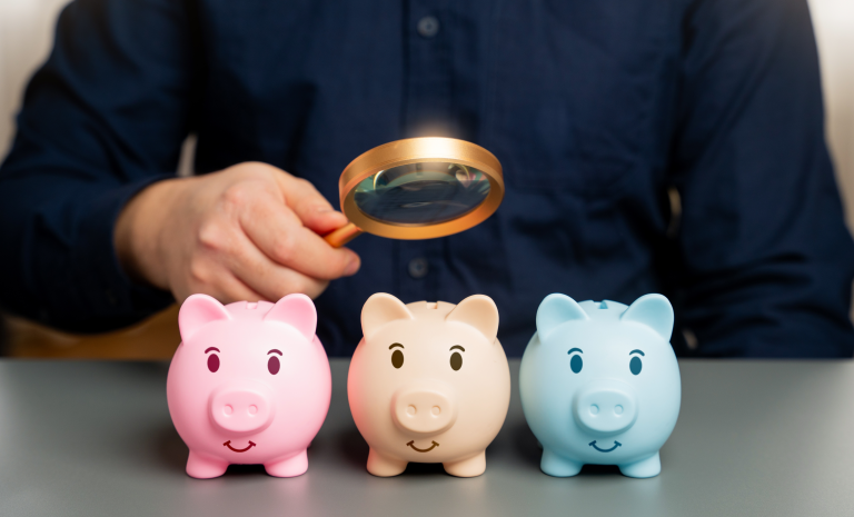 Magnifying glass looks over piggy banks.