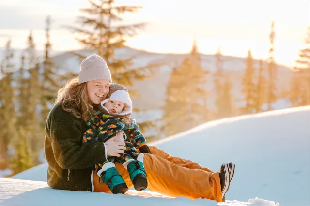 Woman hugging her young child on top of a ski mountain during golden hour.