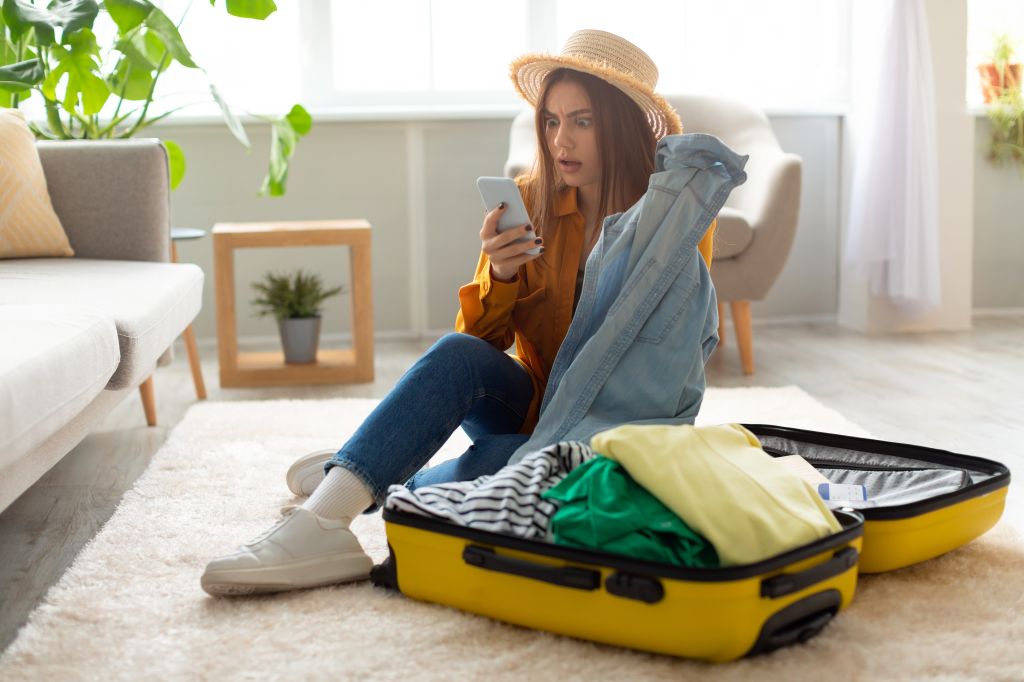 Femme avec un chapeau préparant sa valise pour un voyage tout en regardant son téléphone
