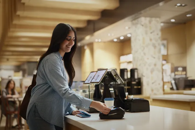 Une nouvelle arrivante sourit tandis qu’elle effleure un terminal de paiement avec sa carte de crédit.